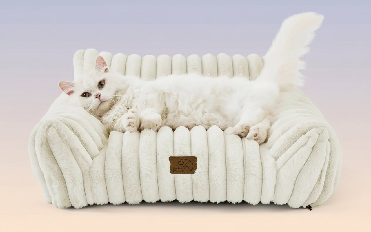 White cat lounging on a plush, white pet bed with a brand logo.